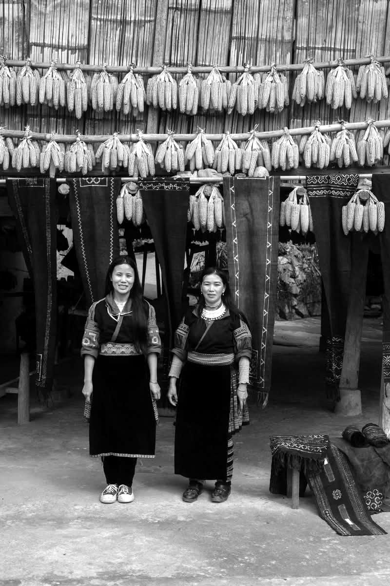 Two Hmong women under rows of hanging corn